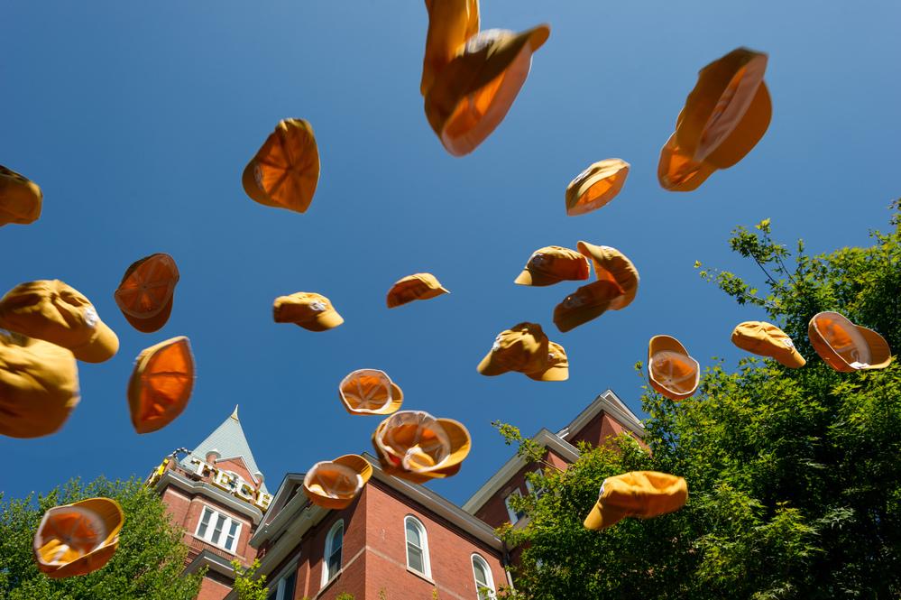 Various yellow caps thrown in the air in front of Tech Tower, as seen from below.