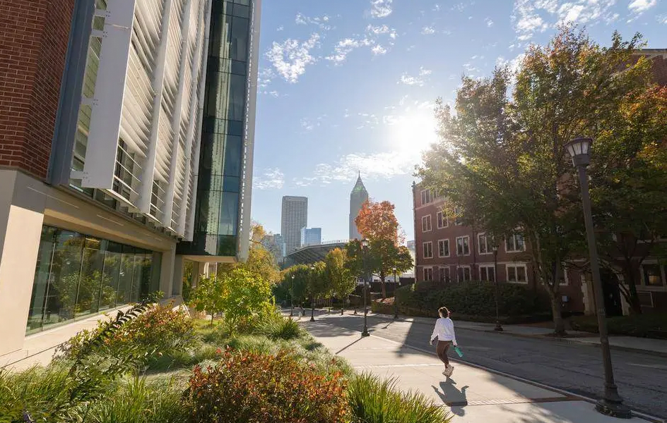 Campus buildings seen from a skyline, a young woman walking with the sun in the background.